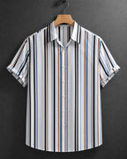 A short-sleeve button-up shirt with vertical stripes in black, white, blue, and brown, hanging on a wooden hanger against a dark gray textured background.