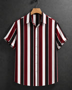 A short-sleeve button-up shirt with vertical stripes in burgundy red, black, and white, hanging on a wooden hanger against a dark gray textured background.