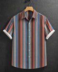 A short-sleeve button-up shirt with vertical stripes in blue, red, brown, and beige, hanging on a wooden hanger against a dark textured background.
