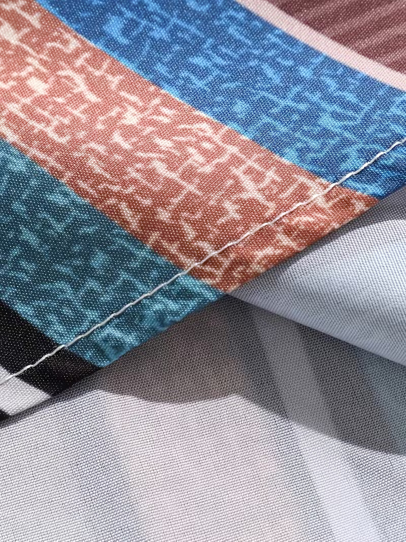 Close-up of a folded patterned fabric with horizontal bands of blue, terracotta, teal, and black, layered over a light gray striped fabric.