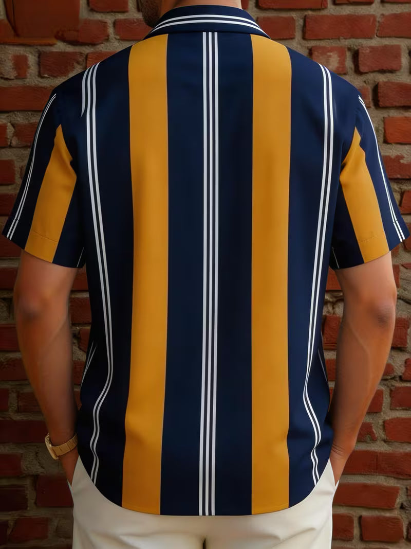 A man viewed from the back wearing a short-sleeve button-up shirt with bold vertical stripes in navy blue, mustard yellow, and thin white stripes, standing against a red brick wall.