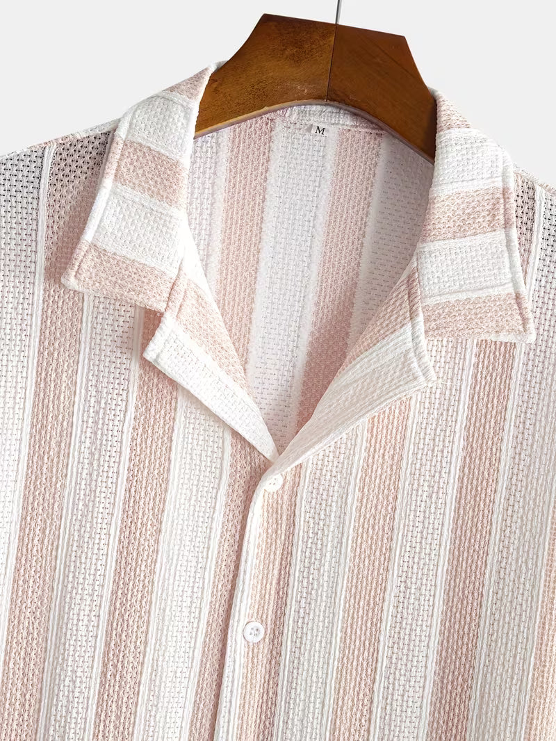 A close-up of a textured knit button-up shirt with vertical stripes in pale pink and white, hanging on a wooden hanger against a light gray background.