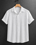 A white short-sleeve button-up shirt with thin vertical gray stripes, hanging on a wooden hanger against a dark gray textured background.