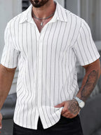 A man wearing a white short-sleeve button-up shirt with thin vertical gray stripes, paired with black pants. The photo is cropped from the chin down, showing his tattooed arm, necklace, and watch.
