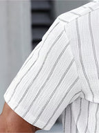 Close-up of a white short-sleeve shirt with thin vertical black pinstripes, worn by a model.