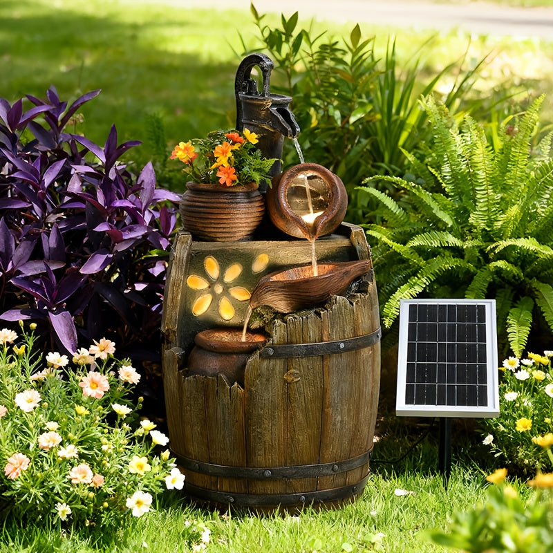 A solar-powered outdoor water fountain shaped like a wooden barrel, with flowing water from a bird-shaped spout, decorative flower cutouts, a small potted plant, and a side-mounted solar panel on a grassy garden bed.