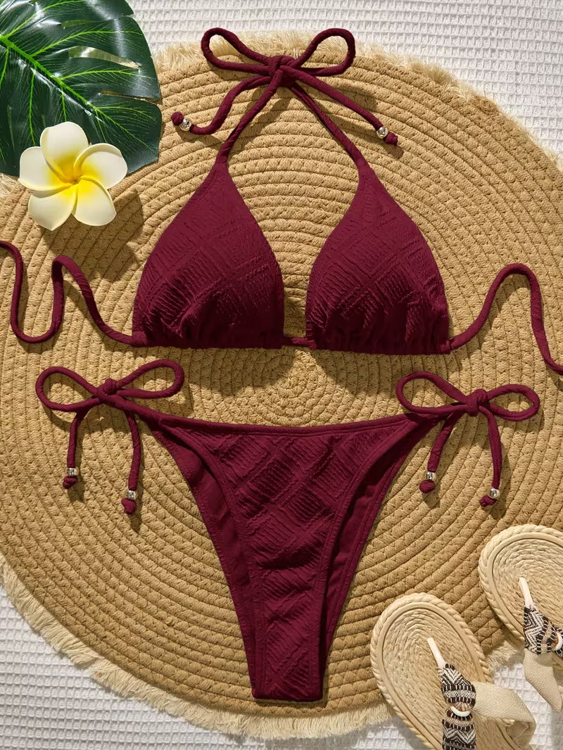 Burgundy bikini set on a woven mat with a flower and hat