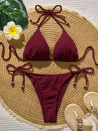 Burgundy bikini set on a woven mat with a flower and hat