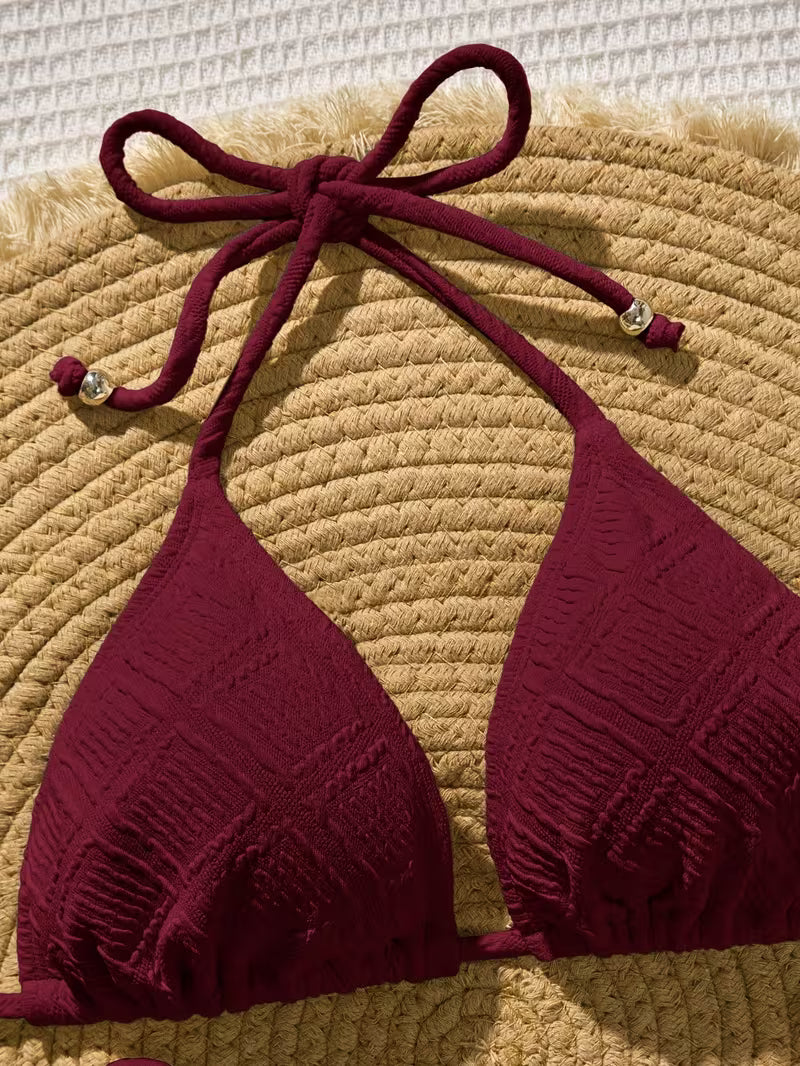 Maroon bikini top with a bow on a textured beige surface