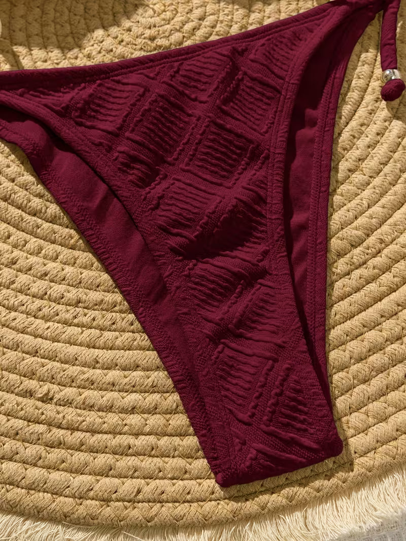 Maroon bikini bottom on a textured beige surface