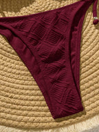 Maroon bikini bottom on a textured beige surface