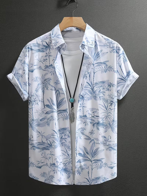 A men's short-sleeve button-up shirt with a blue tropical palm tree and flamingo print on a white background, hanging on a wooden hanger against a dark gray wall.