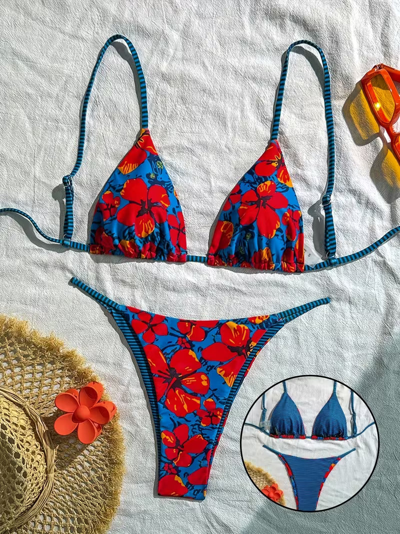 A two-piece bikini set laid flat on a white fabric background, featuring a bold red and blue floral print with blue-and-black striped straps. A circular inset at the bottom right shows a close-up of the bikini top.