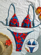 A two-piece bikini set laid flat on a white fabric background, featuring a bold red and blue floral print with blue-and-black striped straps. A circular inset at the bottom right shows a close-up of the bikini top.