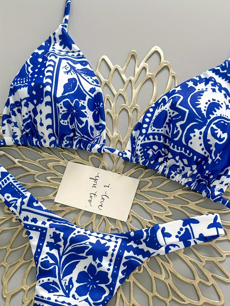 Blue and white patterned bikini set laid flat on a beige woven mat, with a handwritten note card placed on top.