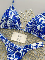 Blue and white patterned bikini set laid flat on a beige woven mat, with a handwritten note card placed on top.