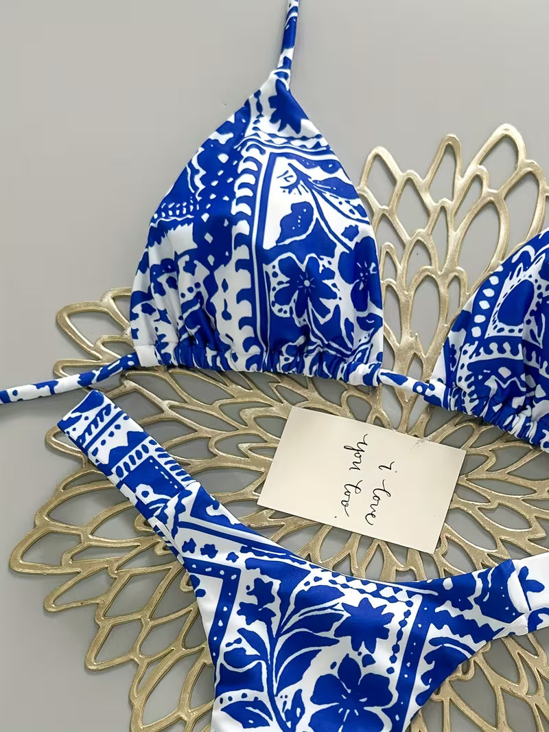 Blue and white patterned bikini set laid flat on a decorative gold metal tray with a handwritten note on top, against a light gray background.