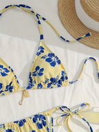 A yellow bikini set with a blue floral print, laid flat on a white surface next to a straw hat.