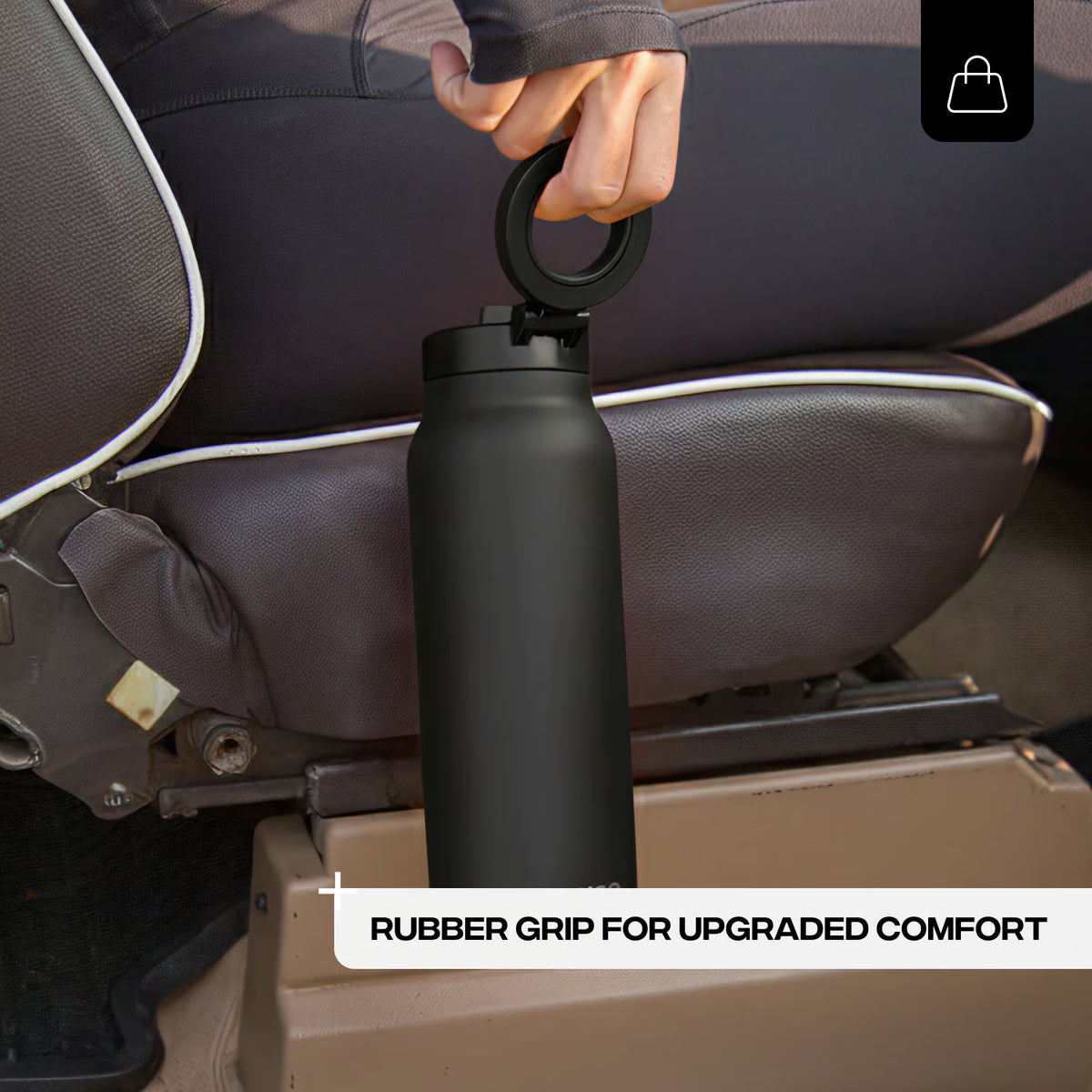 Black water bottle with rubber grip held by a person in a vehicle seat.