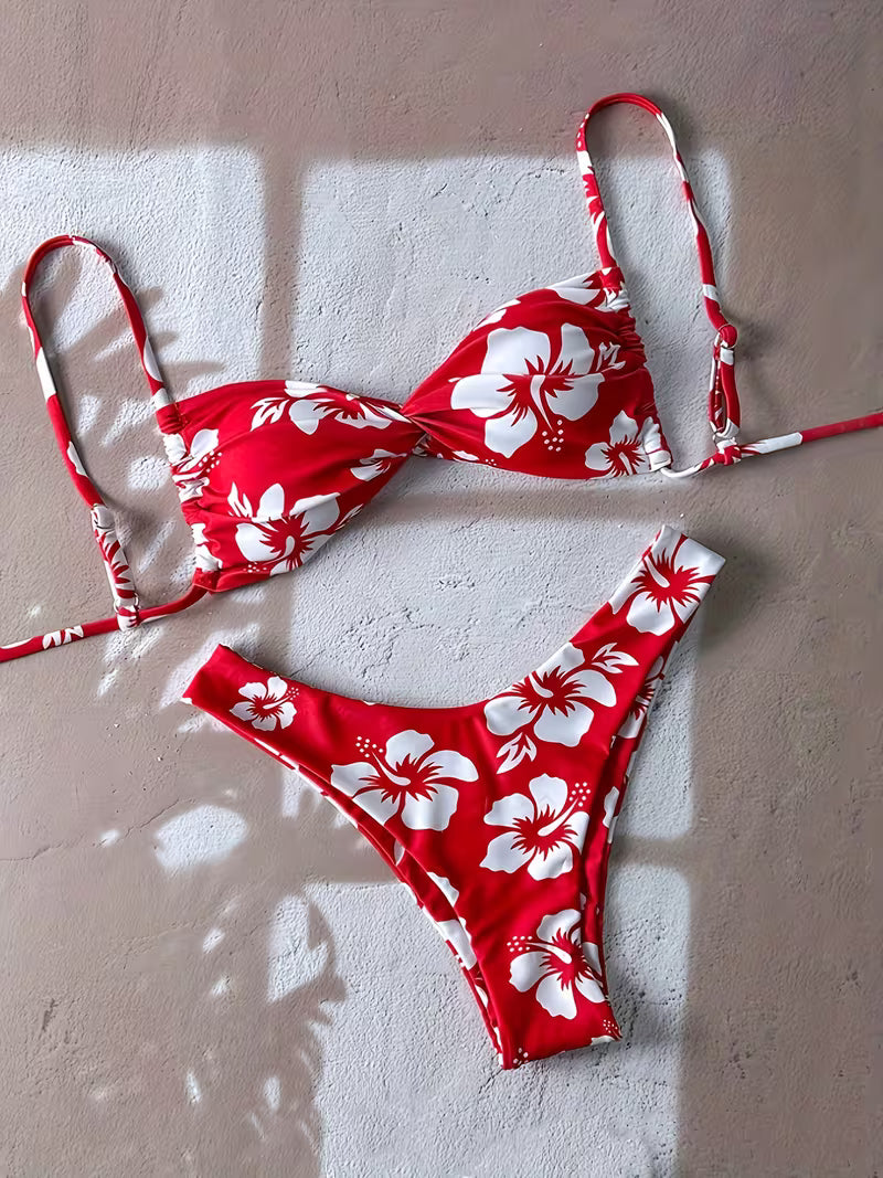 Red and white floral bikini set laid flat on a textured beige wall with soft window shadows.