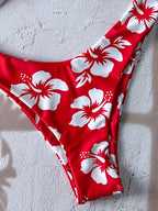 Red bikini bottom with a white hibiscus floral print, laid flat on a textured light gray surface.