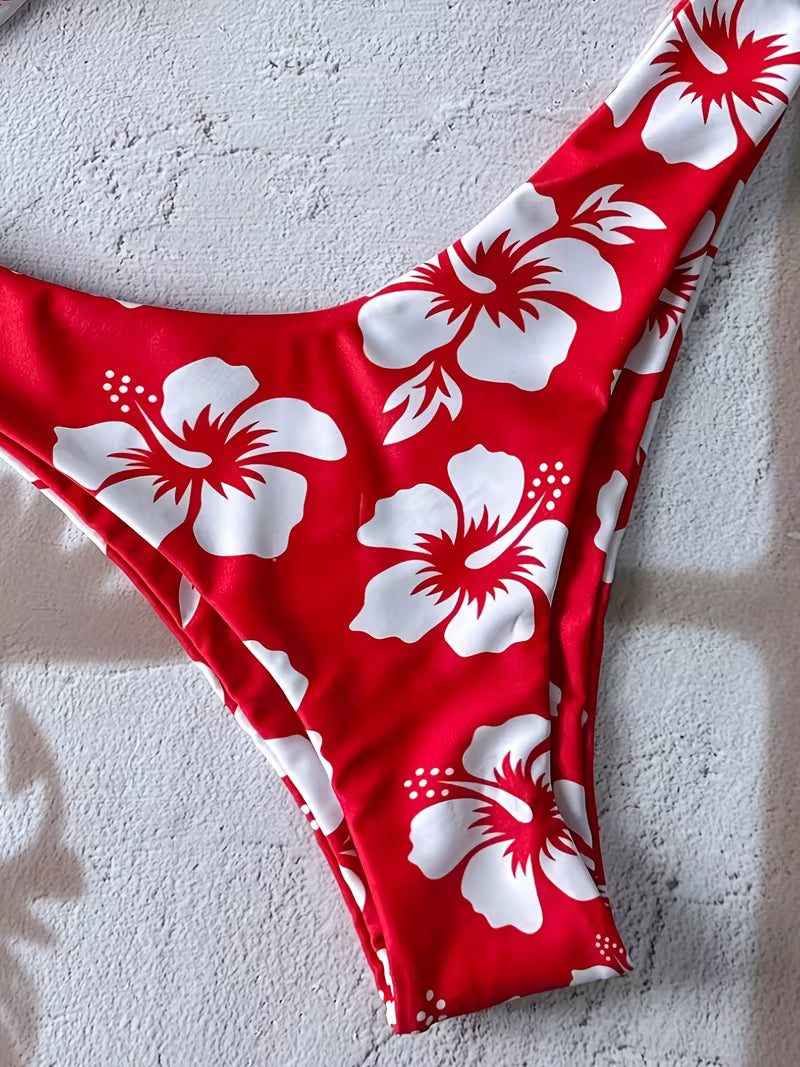 Red bikini bottom with a white hibiscus floral print, laid flat on a textured light gray surface.