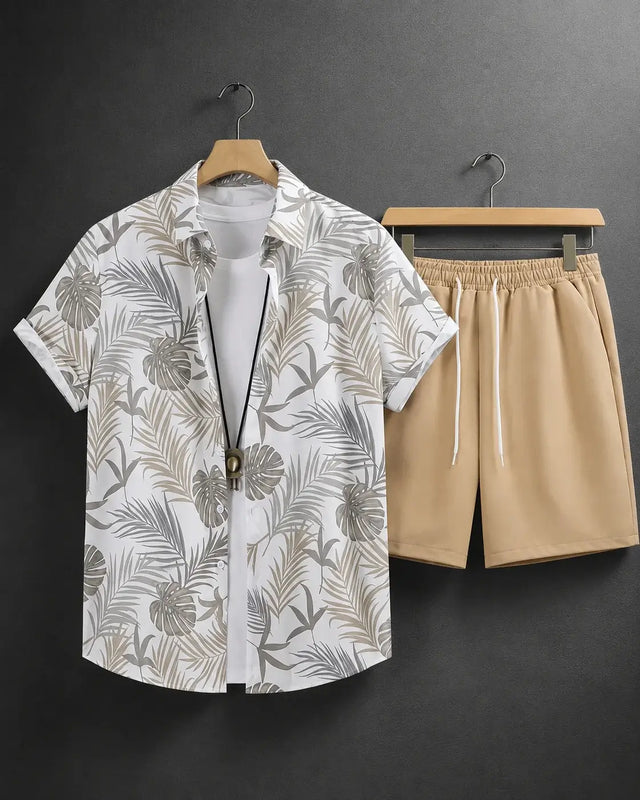 A men's two-piece casual set featuring a white short-sleeve button-up shirt with a gray and beige tropical leaf print, styled over a white undershirt, paired with beige drawstring shorts, hanging on wooden hangers against a dark gray wall.