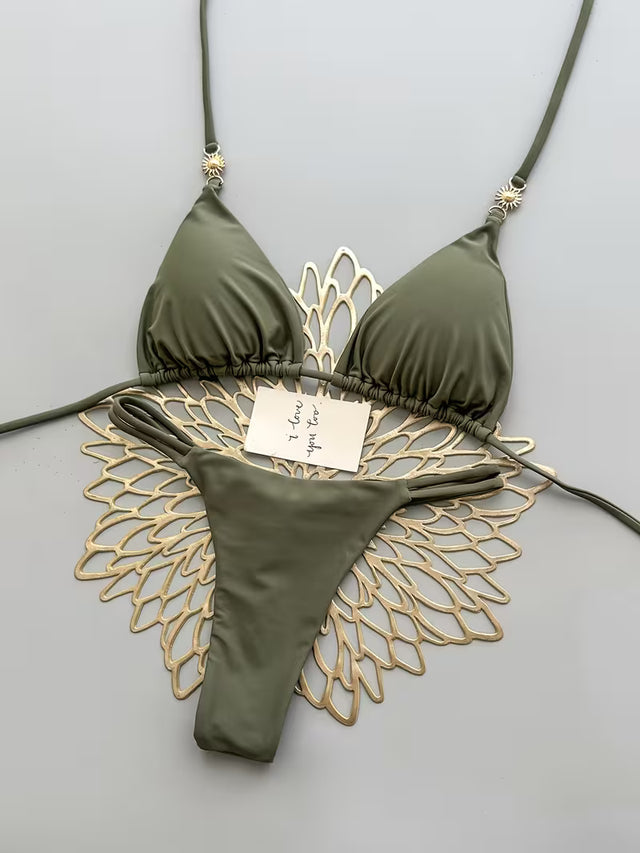 An olive green string bikini set with a decorative gold metallic fish-scale pattern underneath, displayed on a light gray background with a handwritten price tag.