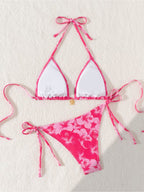 A two-piece bikini set laid flat on a textured off-white background. The top is a triangle halter style with white front panels and bright pink edges, ties, and straps.