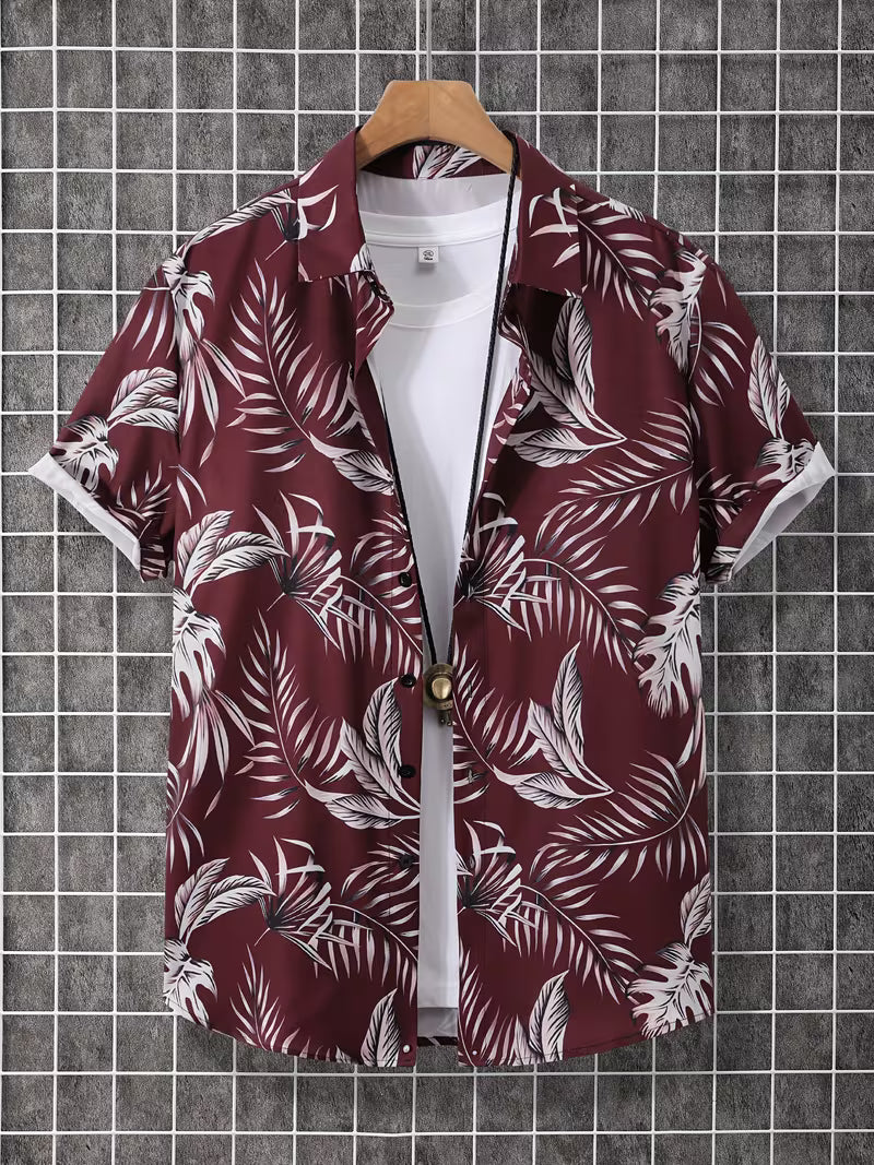 A short-sleeve button-up camp shirt with a white tropical palm leaf pattern on a deep burgundy background, styled over a white t-shirt and hanging on a wooden hanger against a gray grid wall.