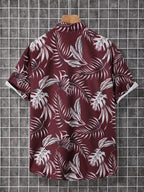 A short-sleeve button-up shirt with a white tropical palm leaf pattern on a deep burgundy background, displayed on a wooden hanger against a gray grid backdrop.