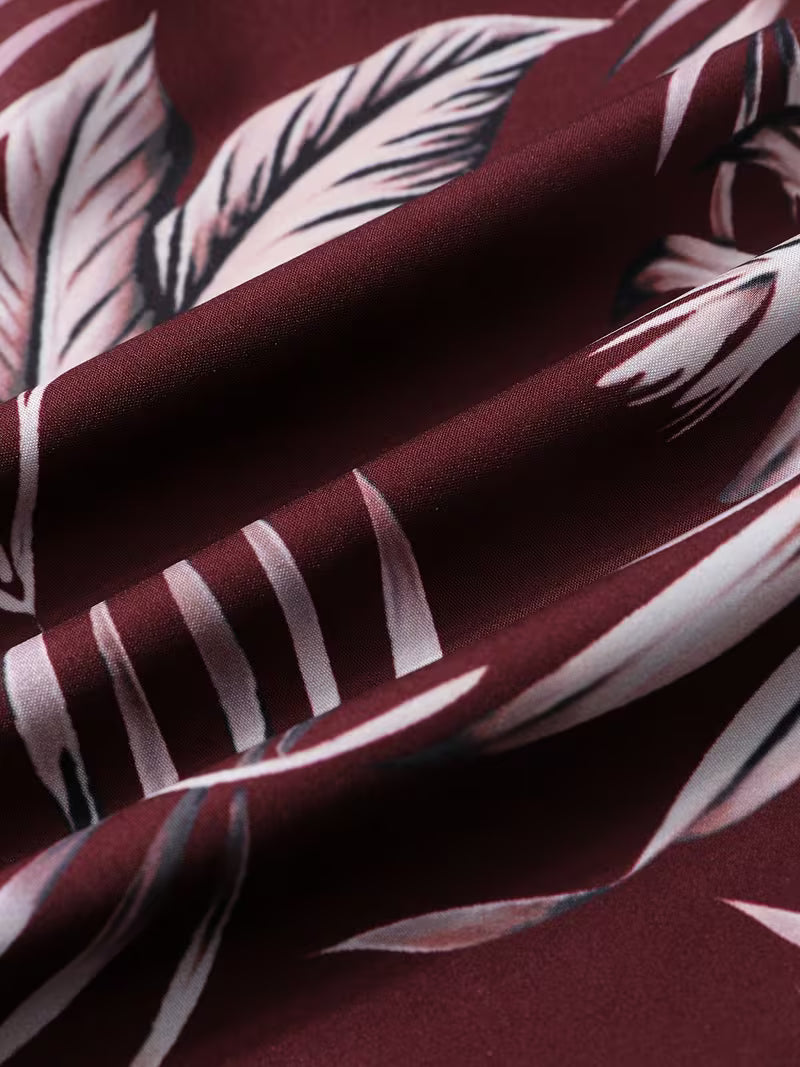 A close-up of draped fabric with a deep burgundy base and a large white tropical leaf print.