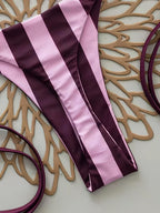 A close-up of a purple and light pink striped fabric garment laid flat on a beige surface with decorative tan cutout shapes and purple loops around it.