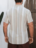 A man viewed from behind wearing a short-sleeve button-up shirt with vertical beige and white stripes, paired with brown pants, standing in front of a white wall and wooden door.