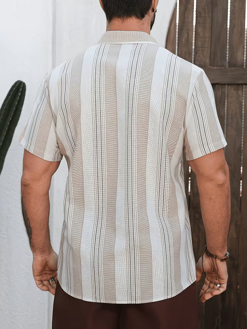 A man viewed from behind wearing a short-sleeve button-up shirt with vertical beige and white stripes, paired with brown pants, standing in front of a white wall and wooden door.