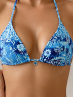 A close-up of a woman wearing a triangle bikini top with a blue and white floral paisley pattern and a small heart-shaped charm at the center front.